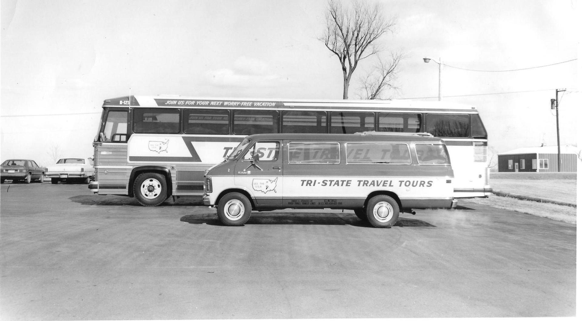 Vintage tour bus and small van parked in a snowy lot, with a leafless tree in the background.