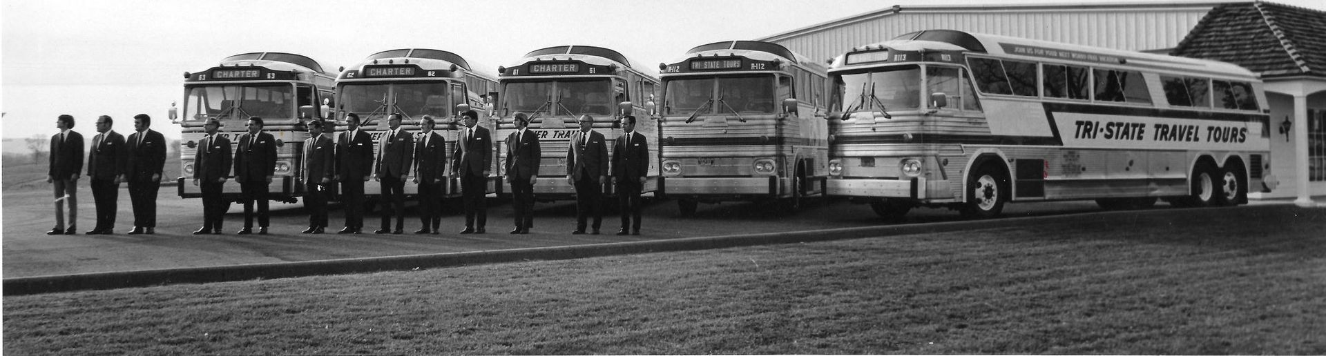 Vintage buses lined up with people standing in front of them on an open field.