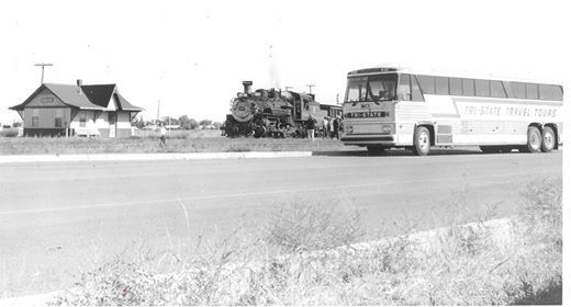 Black-and-white photo of a bus and military vehicle on a road near buildings and grass.