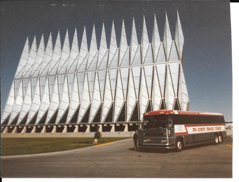 Bus parked in front of a white modern building with pointed roof panels.