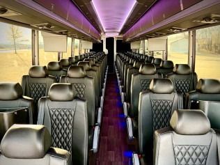 Empty bus interior with black seats, purple ceiling lighting, and large windows