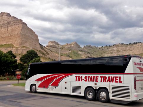 Tri-State Travel tour bus parked beside a rocky mountain road under cloudy skies