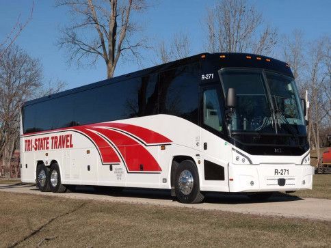 White and red coach bus parked outdoors on a dirt roadside under bare trees