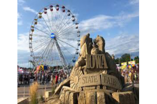Ferris wheel and crowds at the Iowa State Fair entrance sign under a blue sky