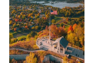Aerial view of a lakeside pavilion and U.S. flag amid autumn trees