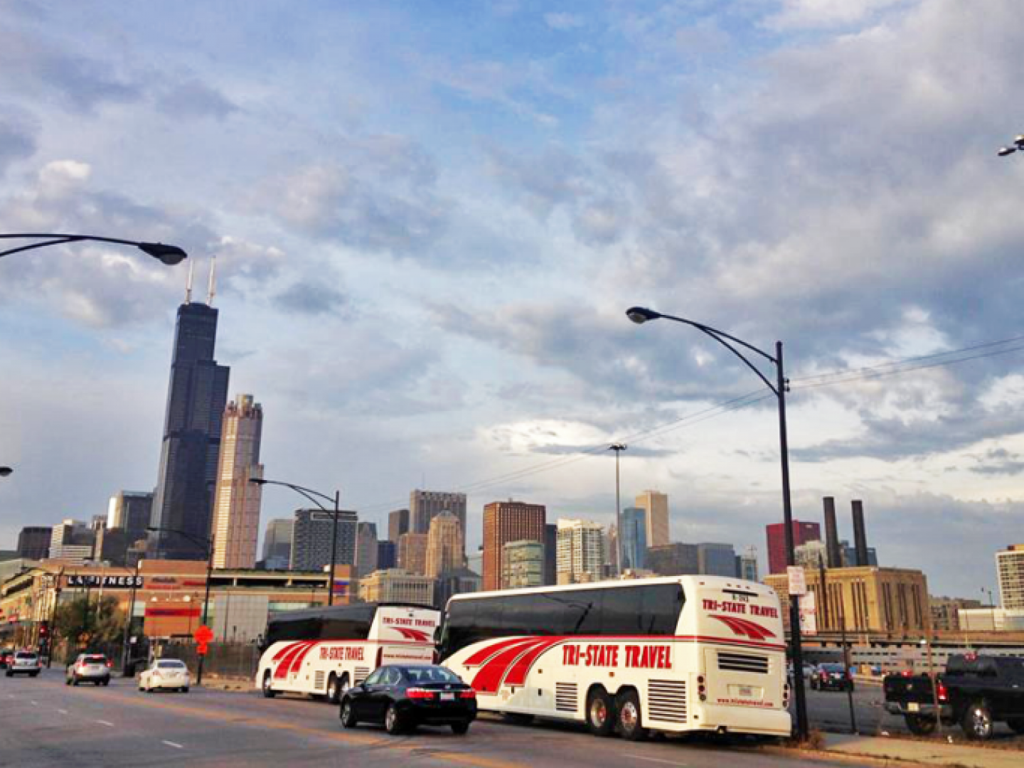 City street with buses and cars under a cloudy sky, skyline in the background
