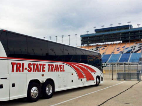 White Tri-State Travel coach bus parked by stadium stands under cloudy sky