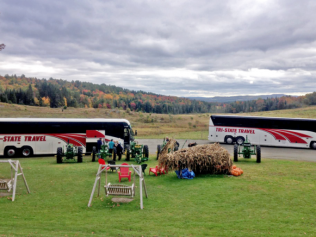 Two buses in a field with a fall landscape, pumpkins, and a small harvest display in the foreground