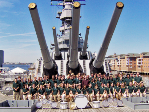 Large group posed on battleship deck beneath giant naval guns under a blue sky