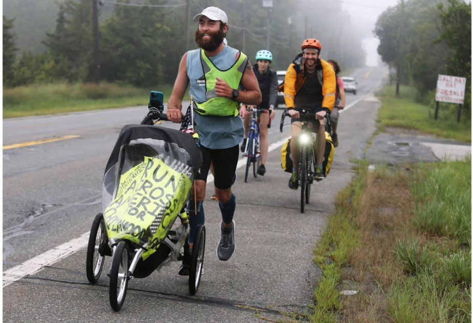 Bearded man runs pushing a stroller with a sign that says