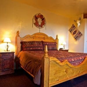 A bedroom with a bed , nightstand , lamps and a bull skull on the wall.