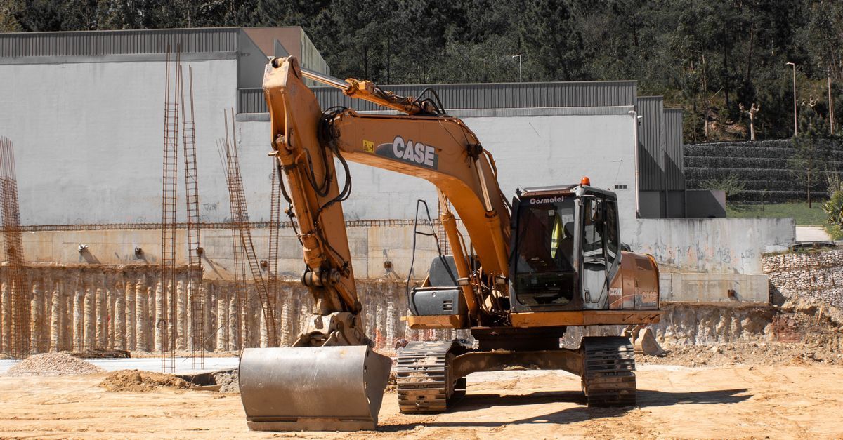Orange excavator moving dirt at a construction site with concrete walls and sandy ground