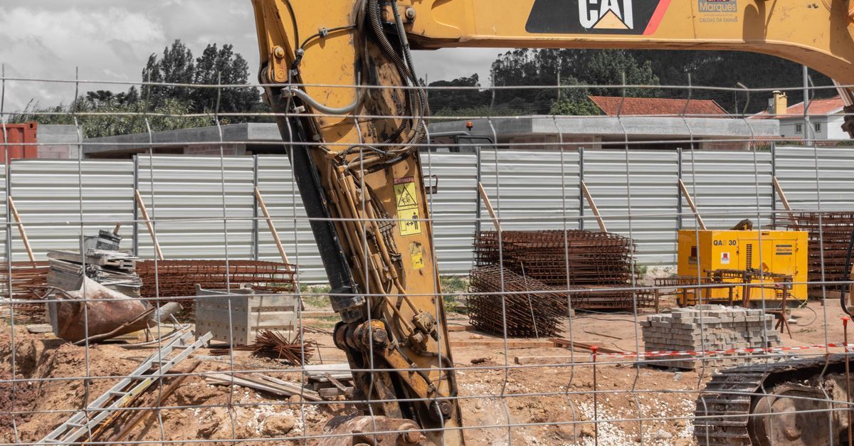 Excavator at a construction site with piles of rubble and temporary fencing behind it