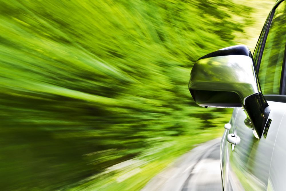 White car driving fast along a blurred green forest road