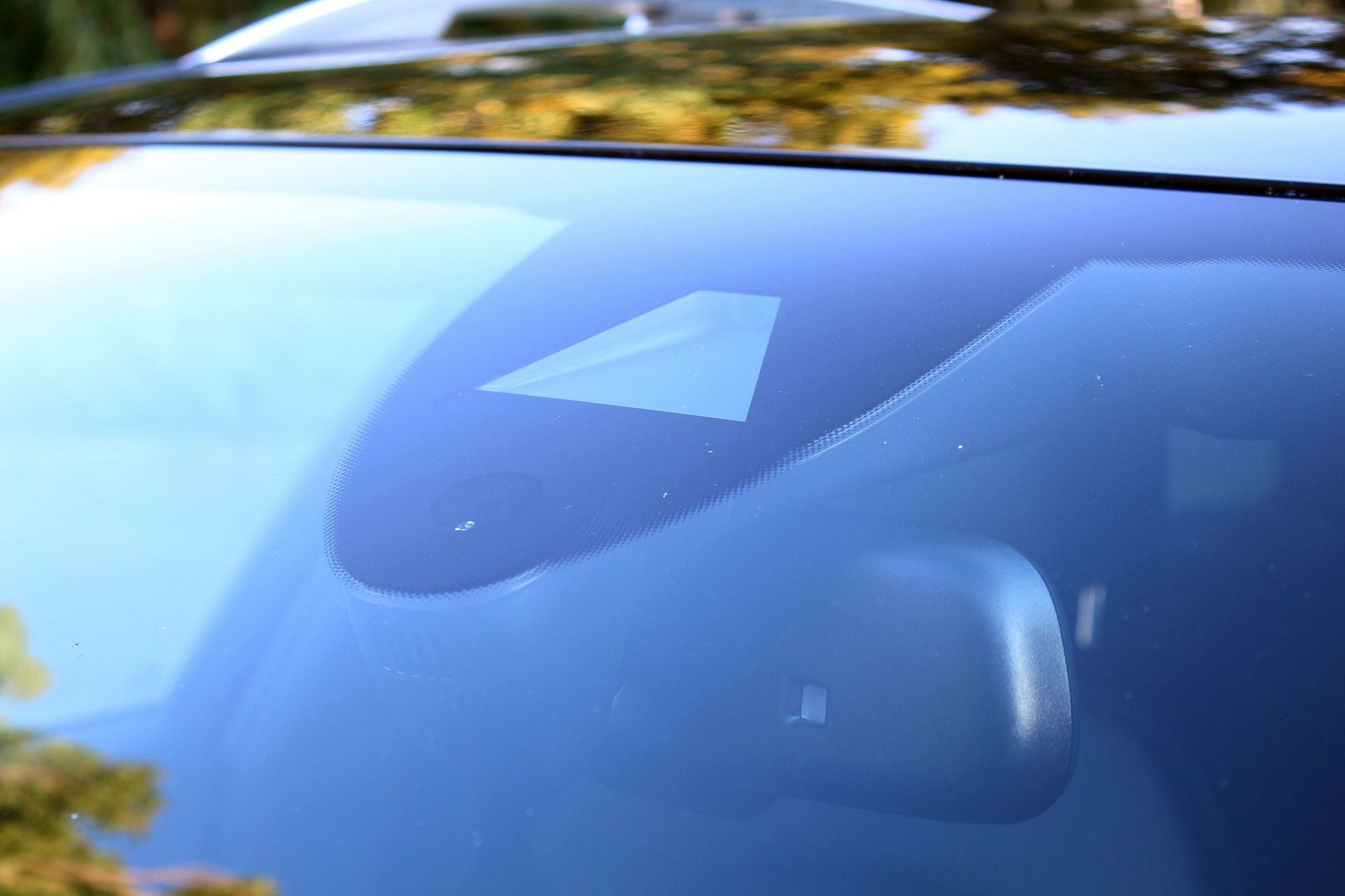 Car windshield reflecting blue sky and trees, with rearview mirror visible inside