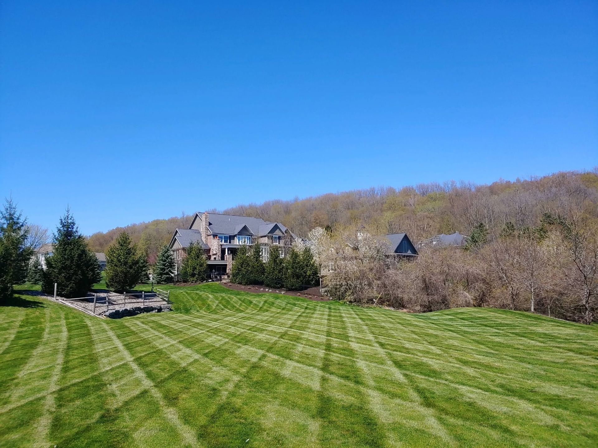 Large stone house on a grassy lawn with trees and hills under a clear blue sky
