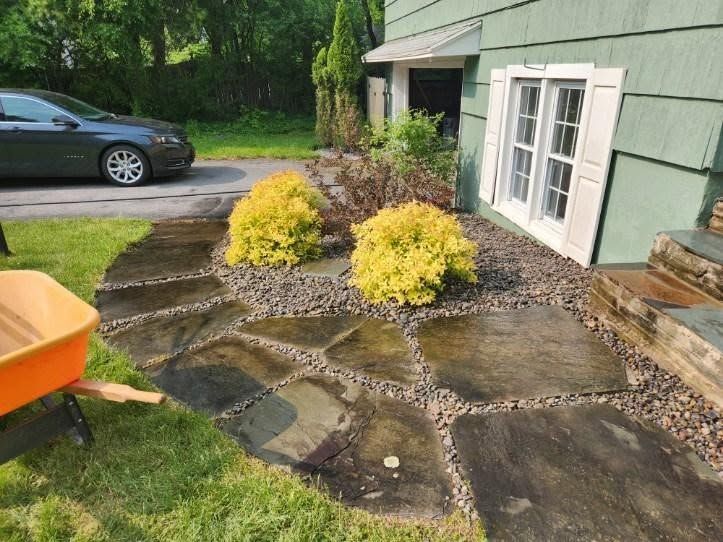 Stone garden path beside green house with yellow shrubs and a parked car in the driveway