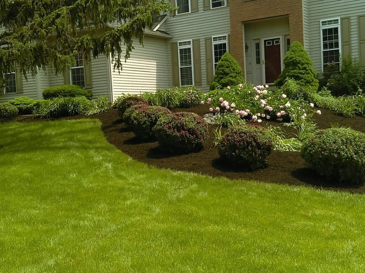Suburban house exterior with a green lawn and landscaped flower beds along the front walkway