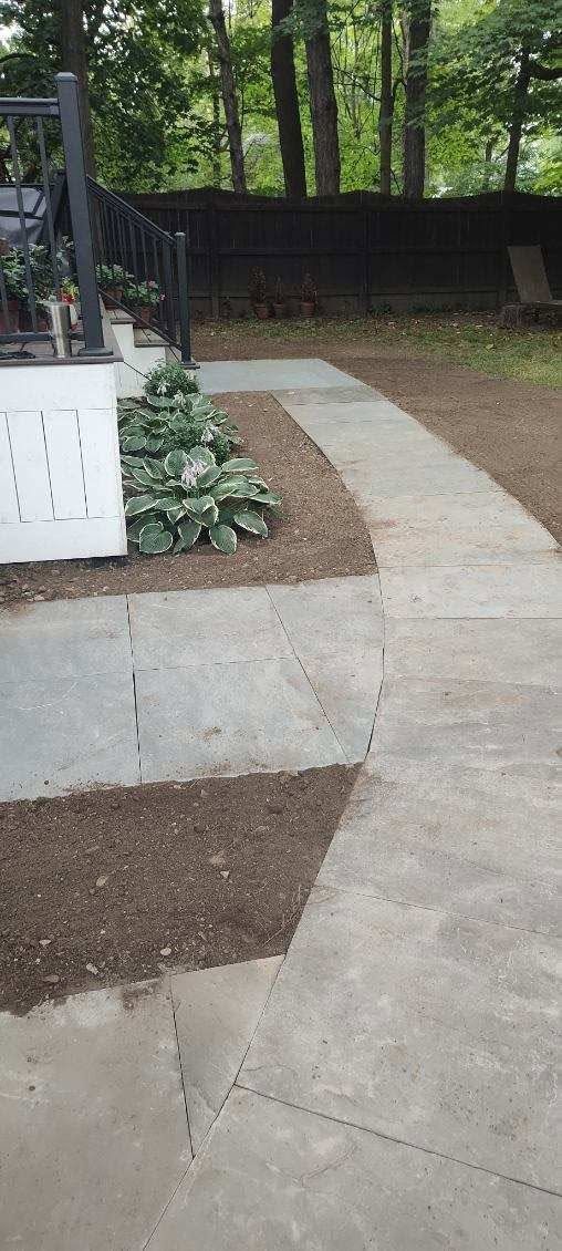 Concrete walkway leading to a backyard patio with trees and a planter bed