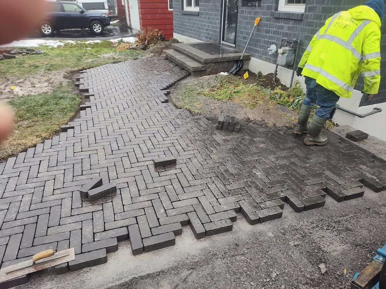 Worker laying gray brick pavers on a curved walkway beside a house