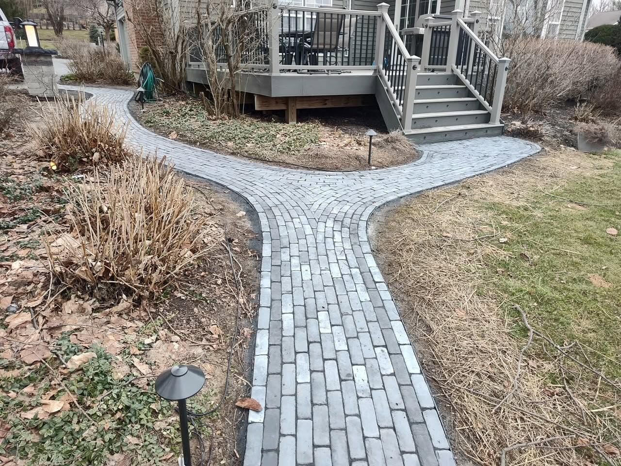 Brick path through a garden leading to a wooden deck and stairs in a backyard.