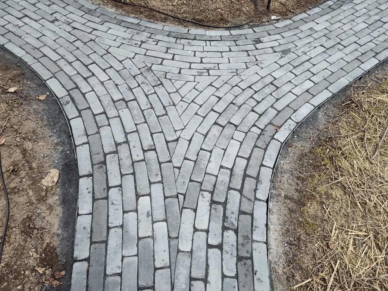 Curved gray cobblestone path junction surrounded by bare soil and dry grass