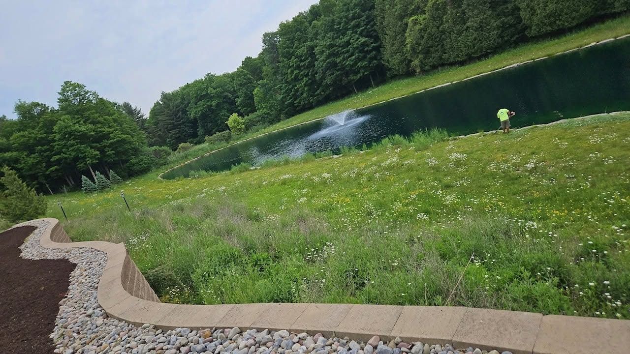 Grassy hillside with a hedge, gravel path, and small fountain under a cloudy sky.