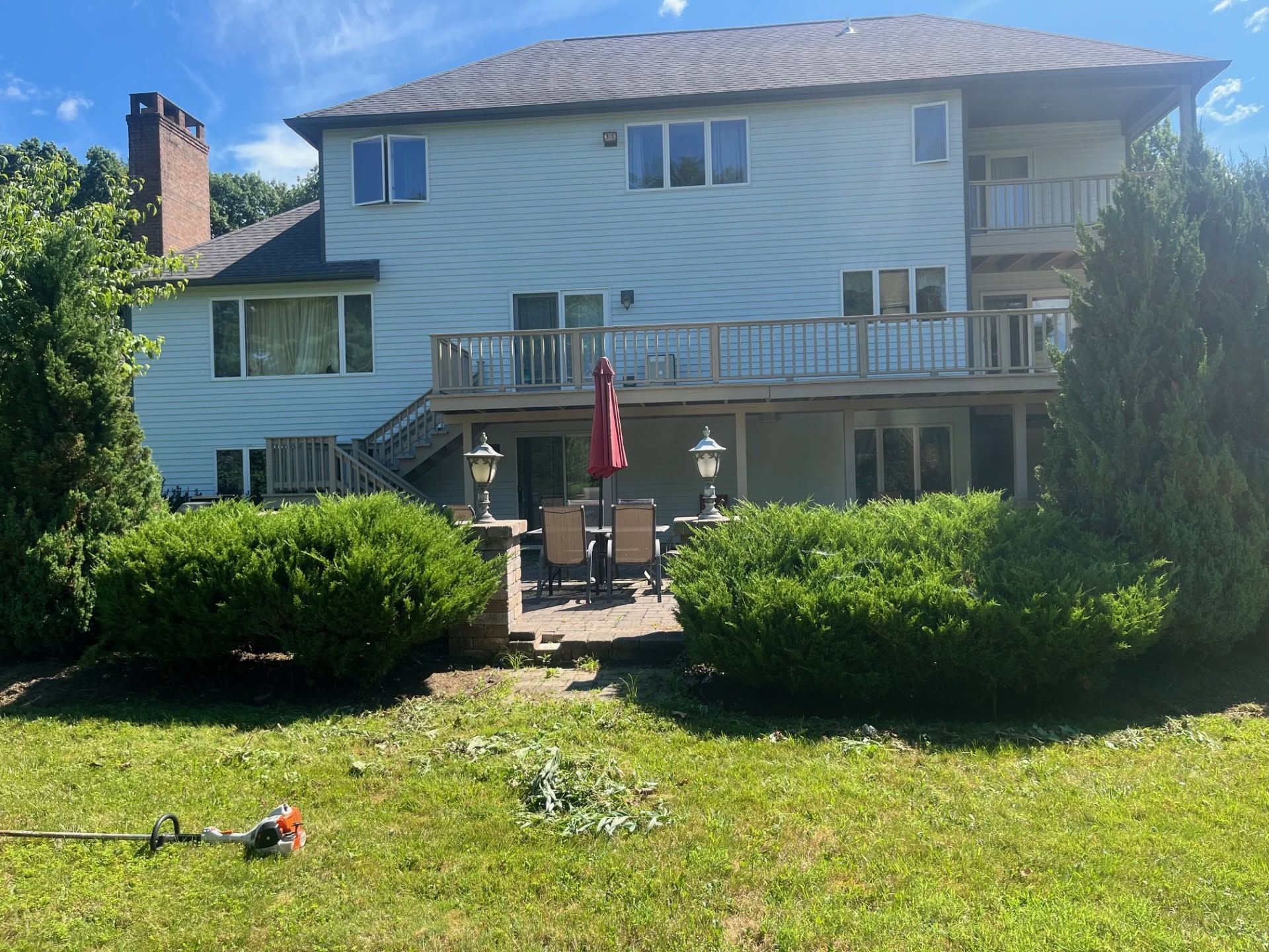 Backyard view of a two-story house with deck, patio umbrella, and green lawn in bright sunlight