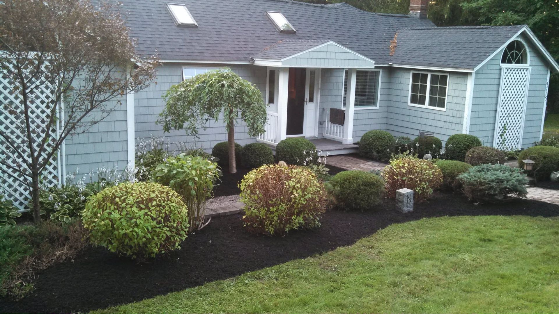 Suburban house with gray siding, white trim, and landscaped front yard with shrubs and lawn