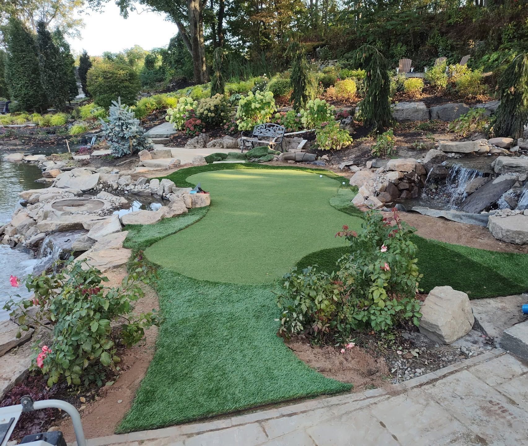 Landscaped backyard mini golf area with artificial turf, rocks, and lush greenery