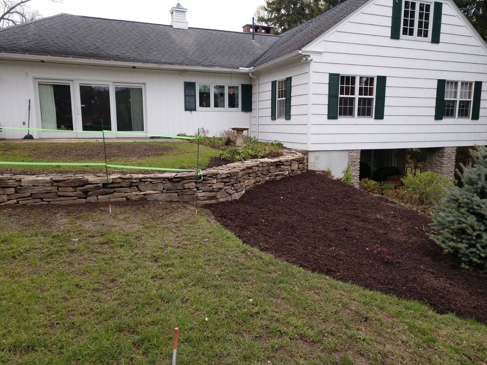 White house with raised deck above a landscaped backyard and stone retaining wall