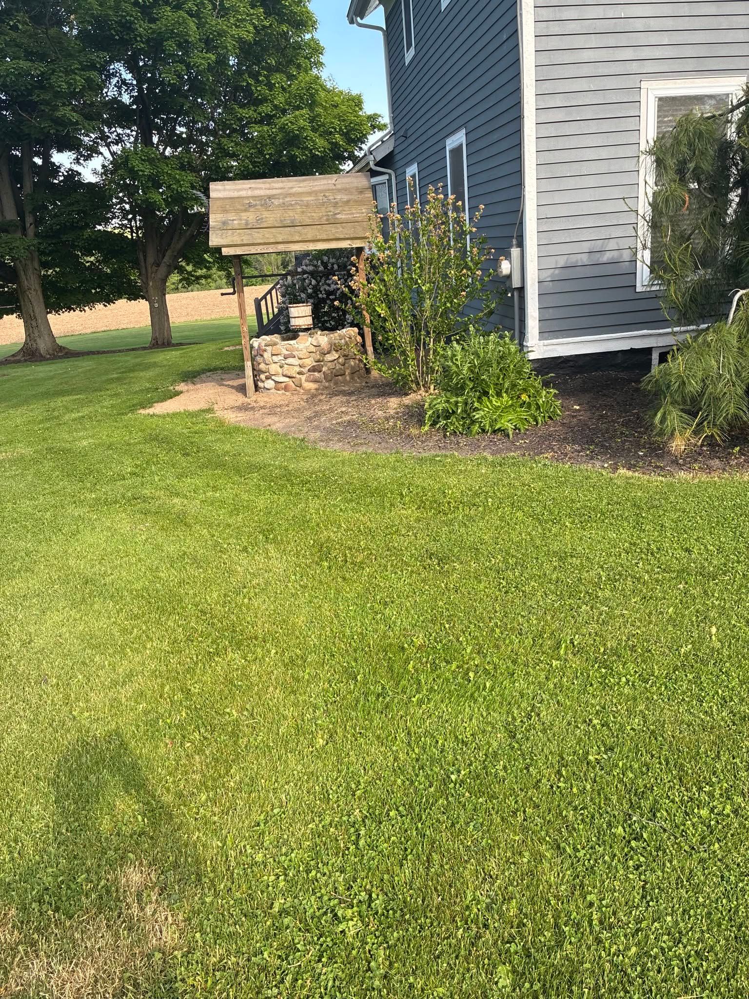 Backyard with a stone garden well beside a house, surrounded by green lawn and shrubs.