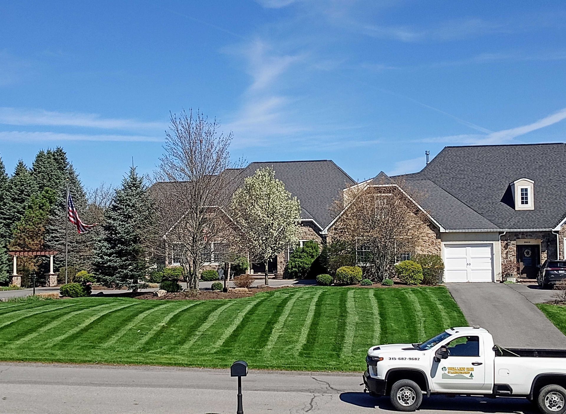 Lawn care truck parked on a street in front of striped lawns and houses under a blue sky.