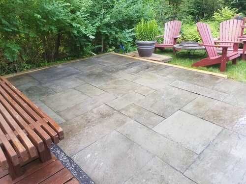 Stone patio with wooden benches and Adirondack chairs in a green garden setting