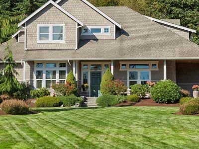 Two-story house with manicured lawn and landscaping.  Gray siding, white trim, green door, and neatly mowed grass.