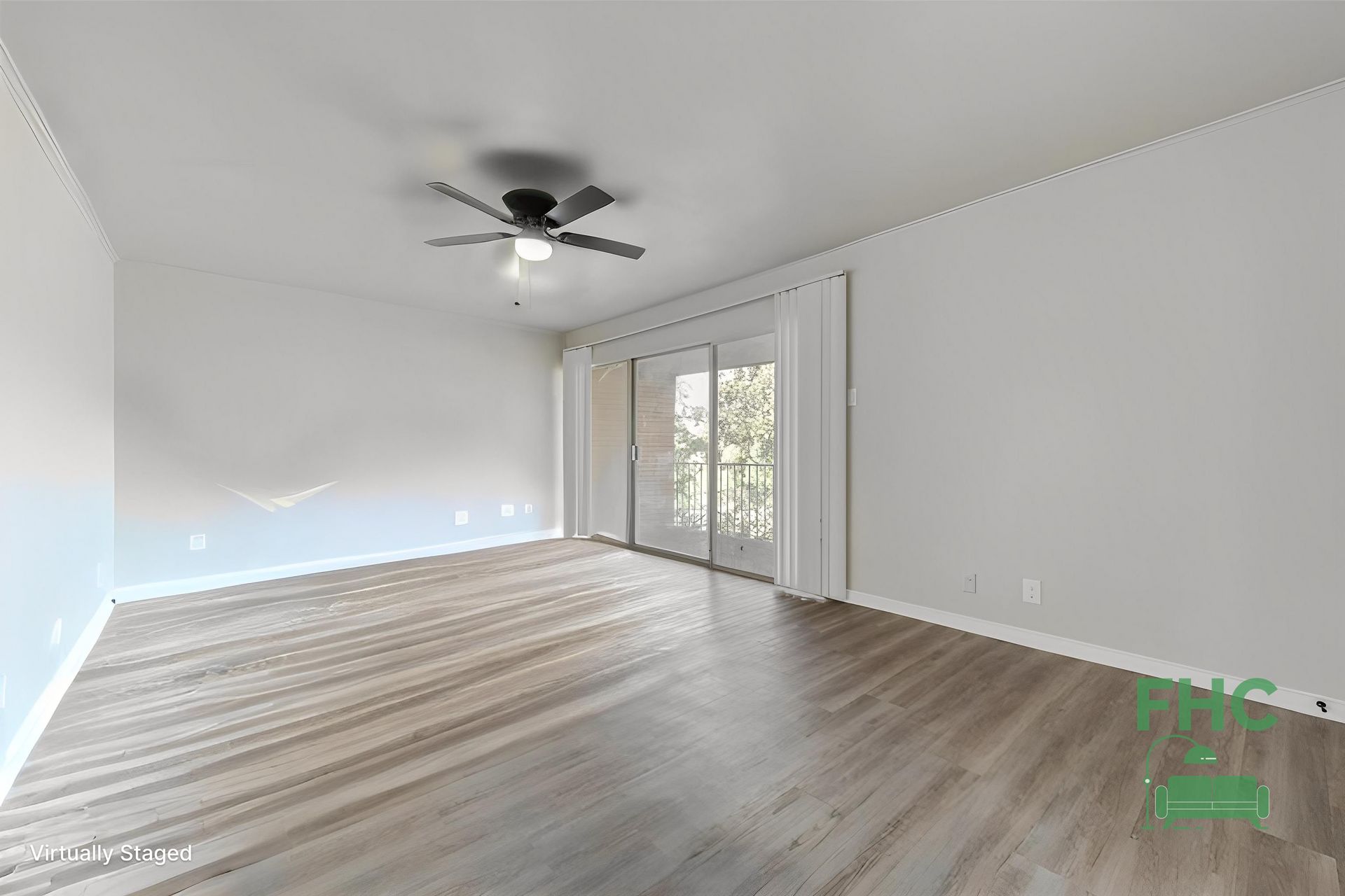 Empty room with gray-brown wood floors, white walls, and a sliding glass door leading to a balcony.