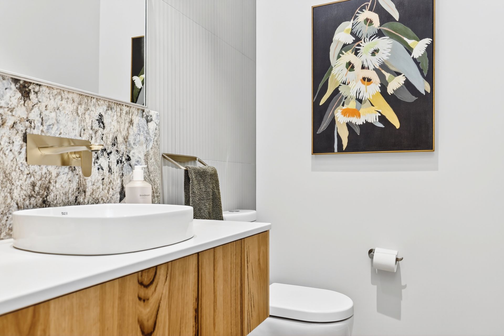 Bathroom with marble sink, wooden cabinet, and floral painting on white wall.