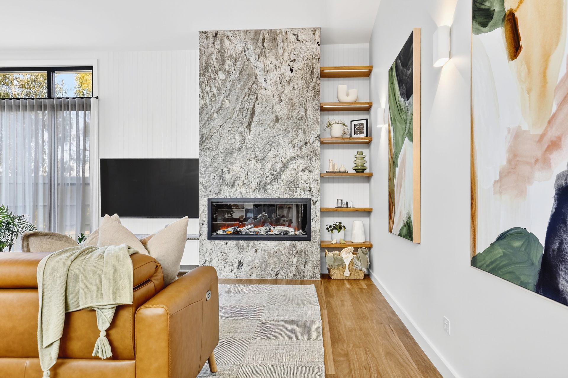 Living room with a stone fireplace, wood shelves, and tan leather sofa.