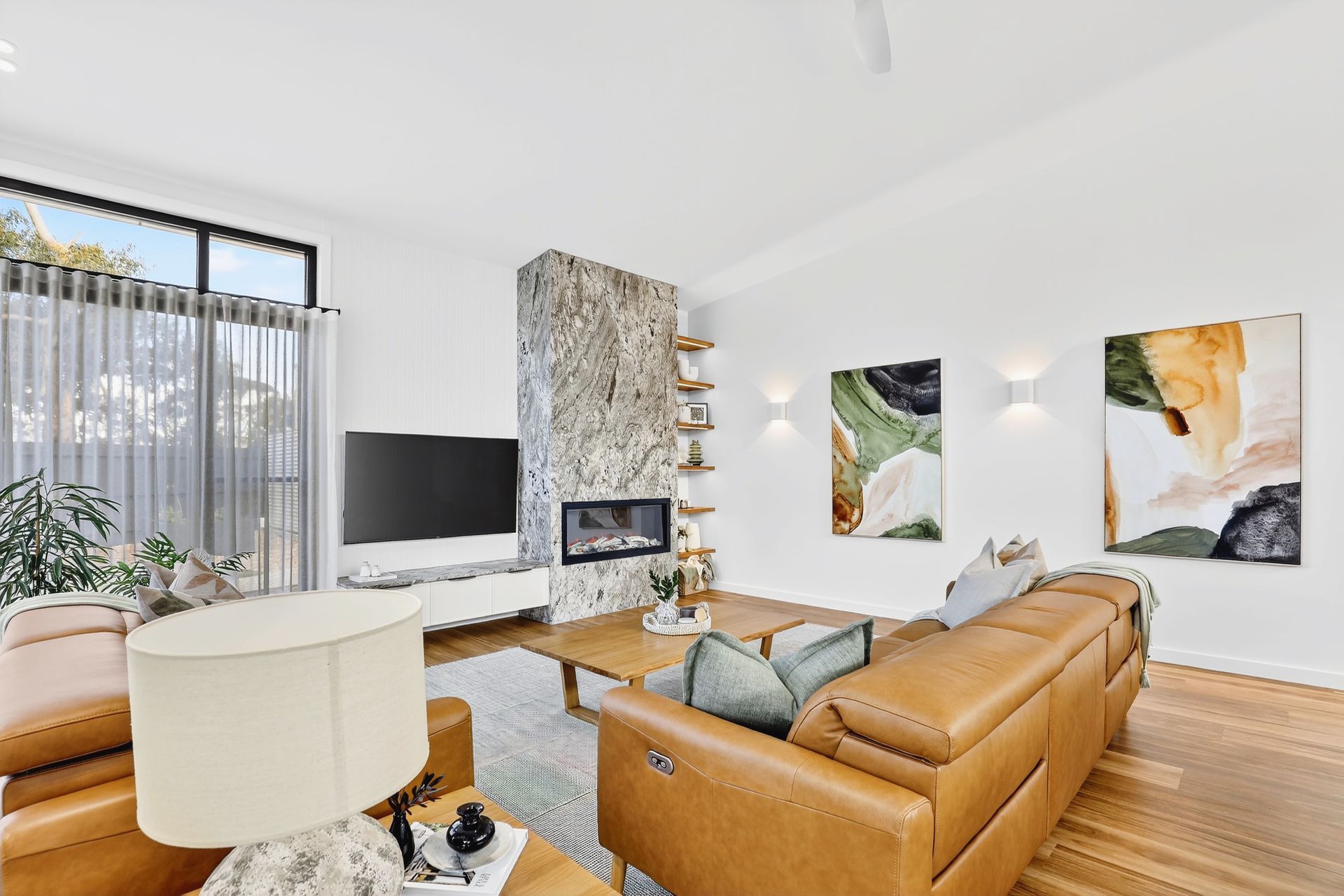 Living room with tan leather furniture, a fireplace, and artwork on a white wall.