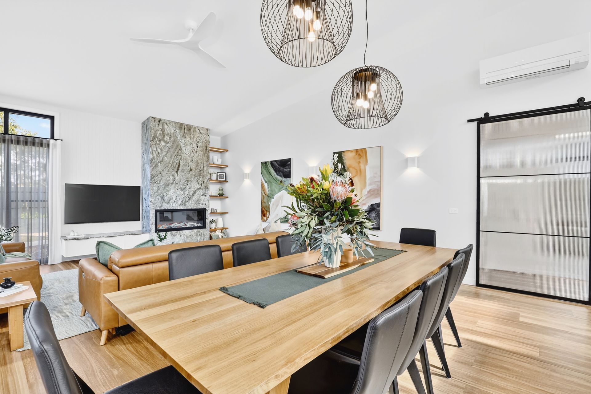 Modern dining and living room with a wooden table, leather sofa, fireplace, and decorative lighting.