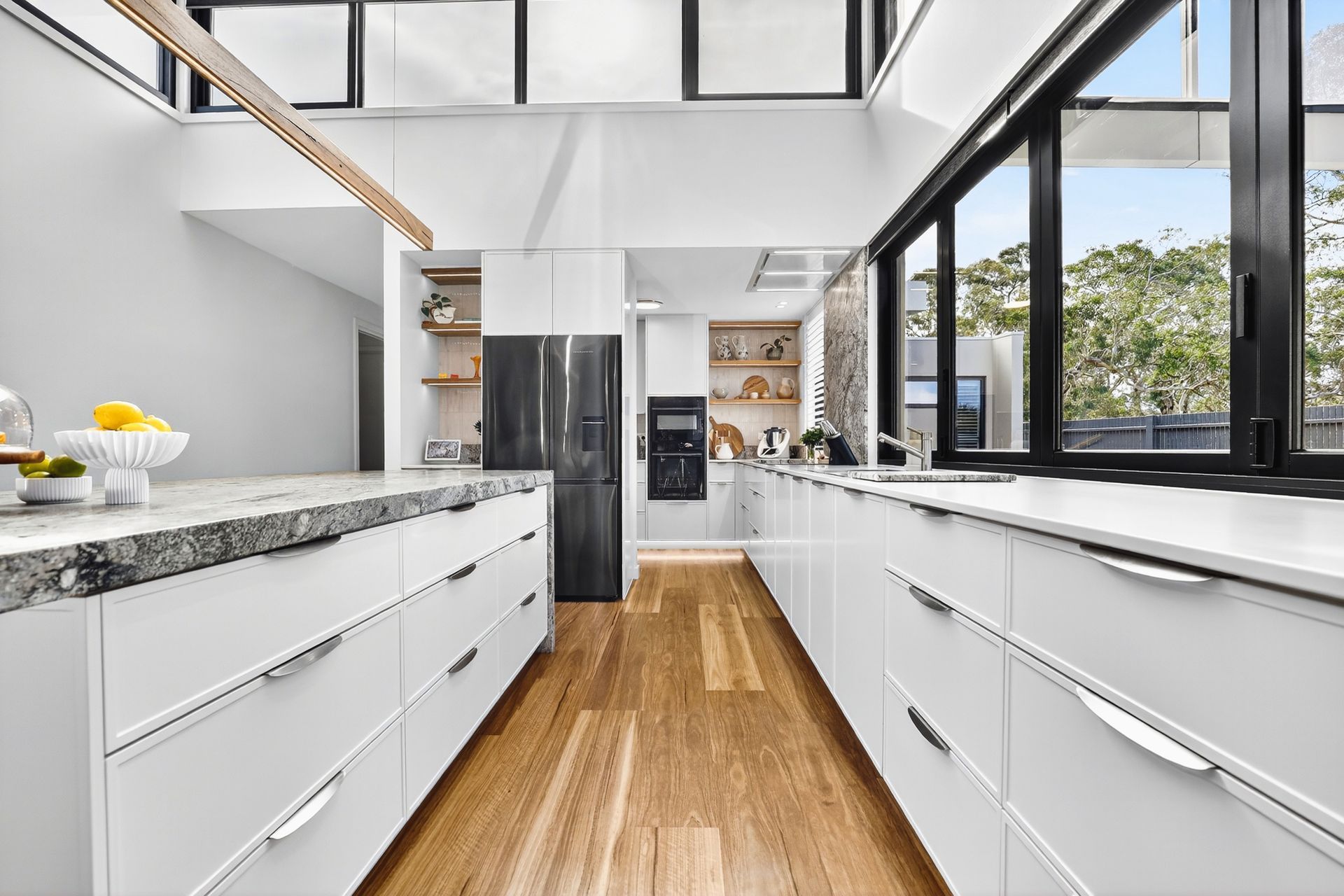 Modern kitchen with white cabinets, granite countertops, black windows, and wood floors.
