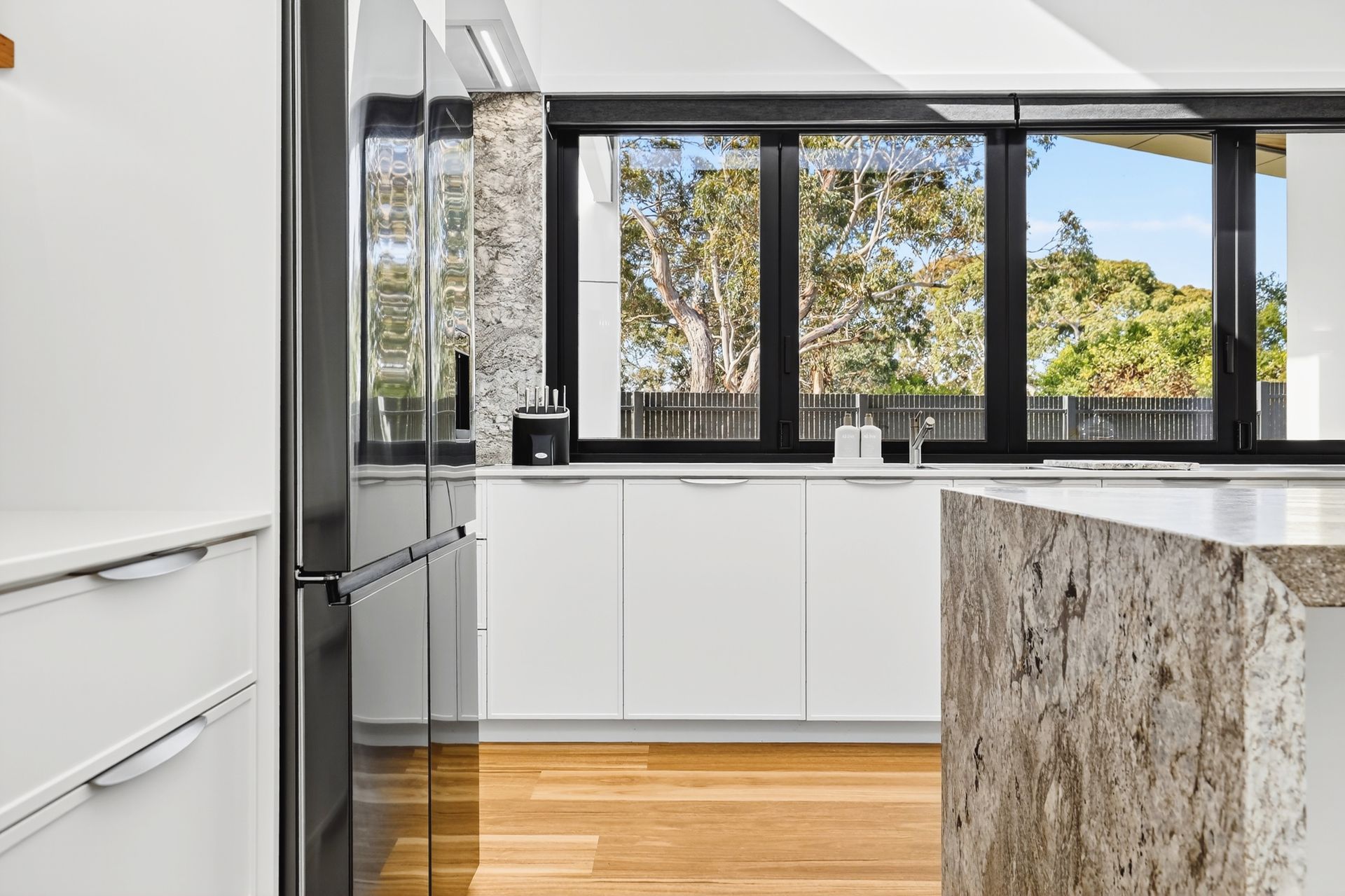 Modern kitchen with white cabinets, black trim windows, granite island, and a large refrigerator.