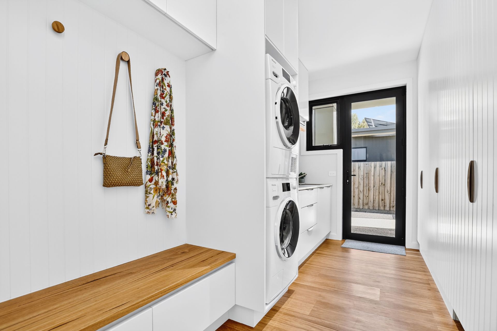 Laundry room with stacked washer/dryer, bench, and door to outside.