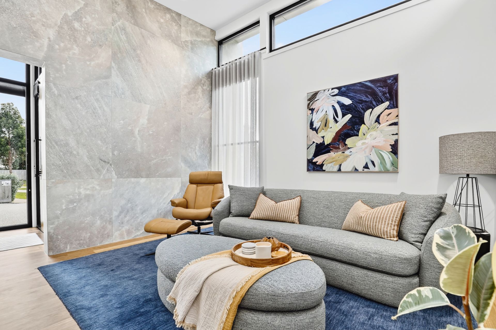 A modern living room with grey couch, blue rug, stone wall, and artwork.