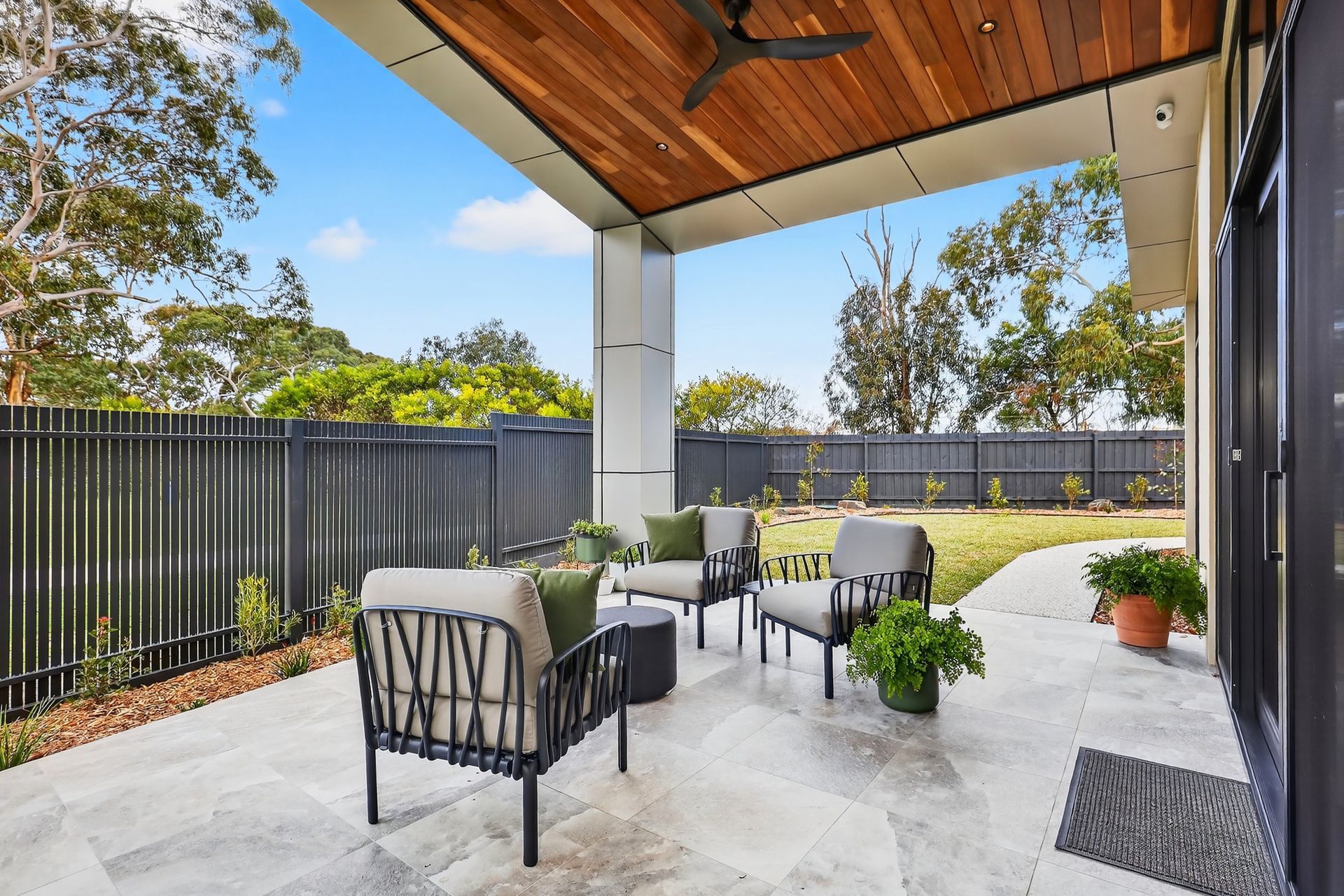 Patio with seating area, wood ceiling, and gray stone flooring. Overlooks a backyard with fence.