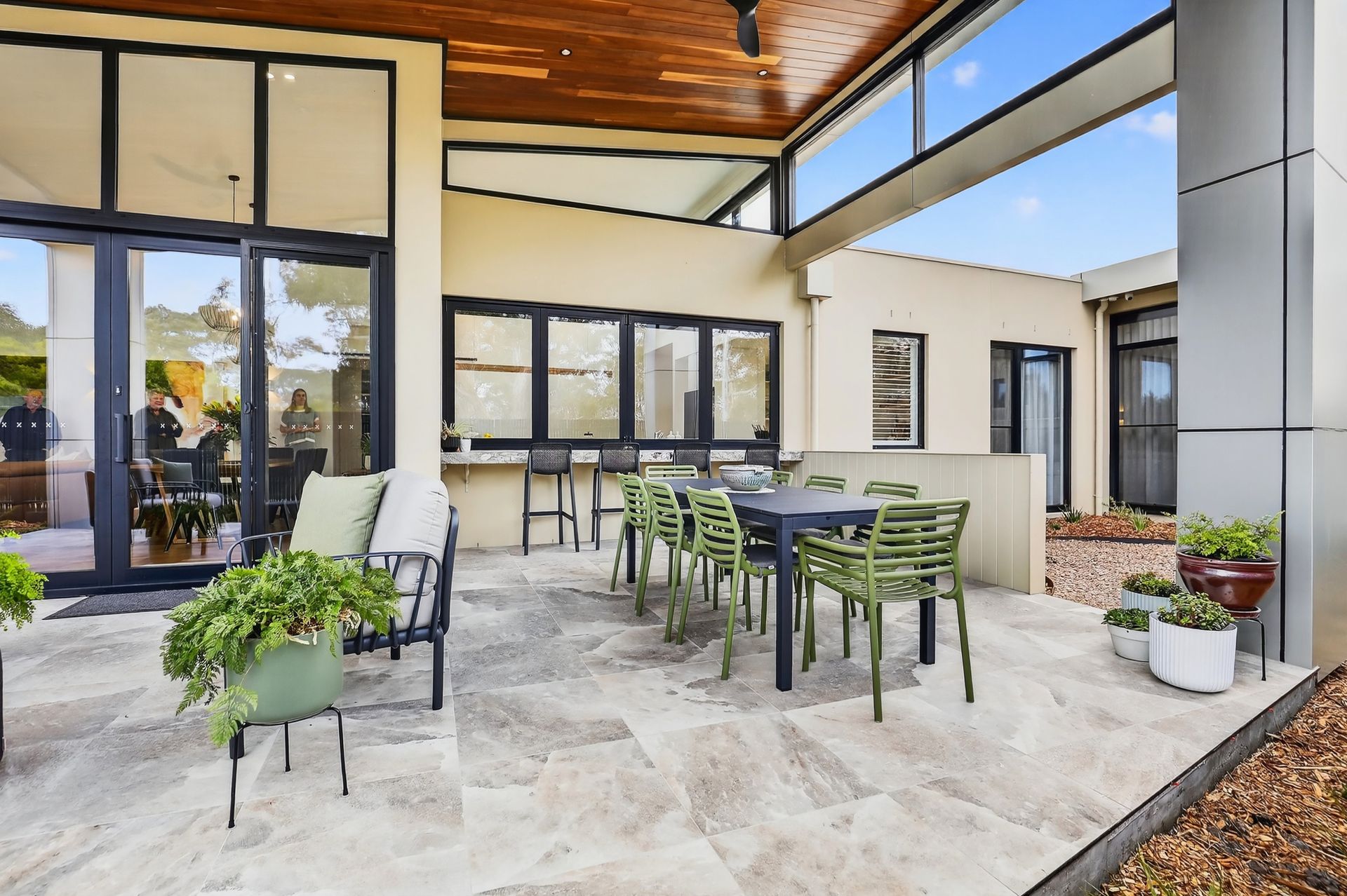 Outdoor patio with a dining table, green chairs, and bar seating under a wood-paneled ceiling.