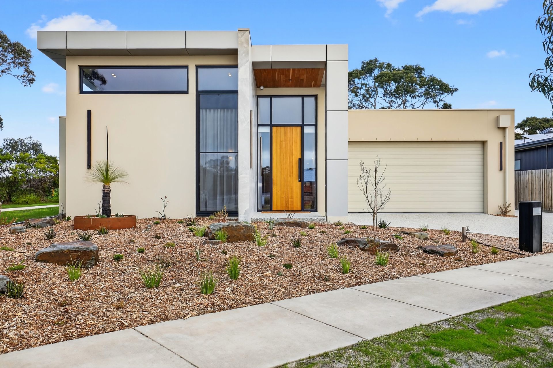 Modern beige house with a wooden door, garage, and landscaped yard with gravel.