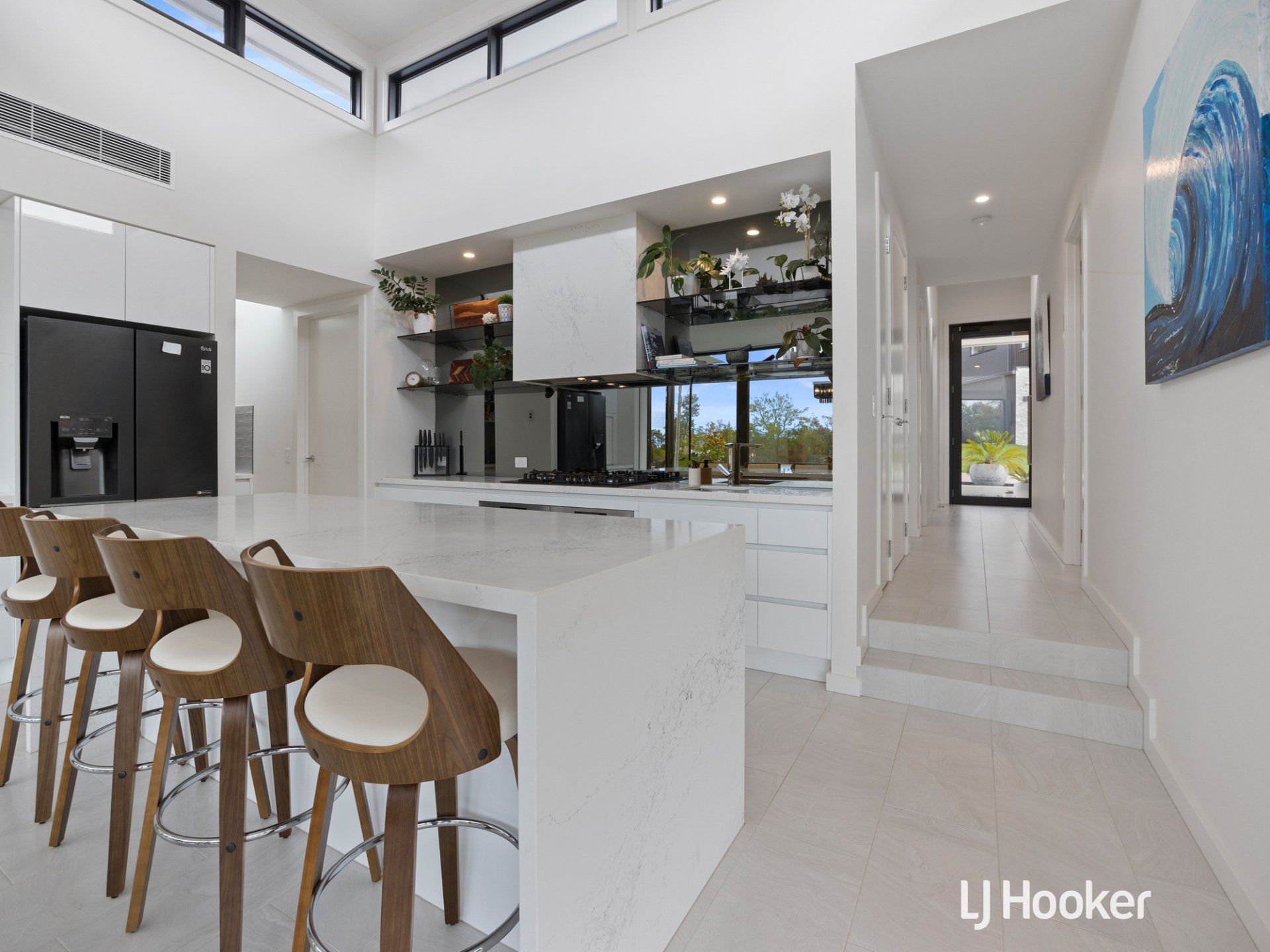 A kitchen with a large island , stools and a refrigerator.