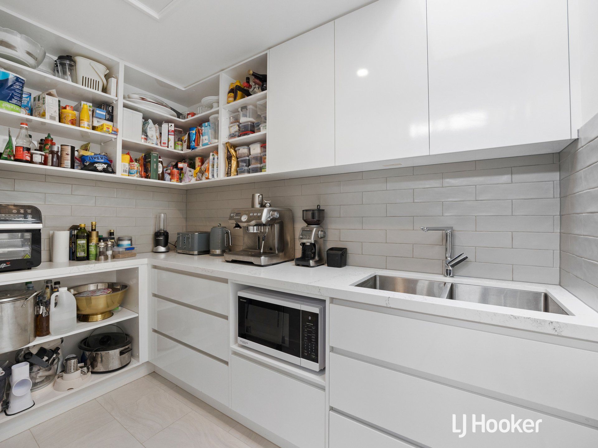 A kitchen with white cabinets , a sink , a microwave , and a pantry.