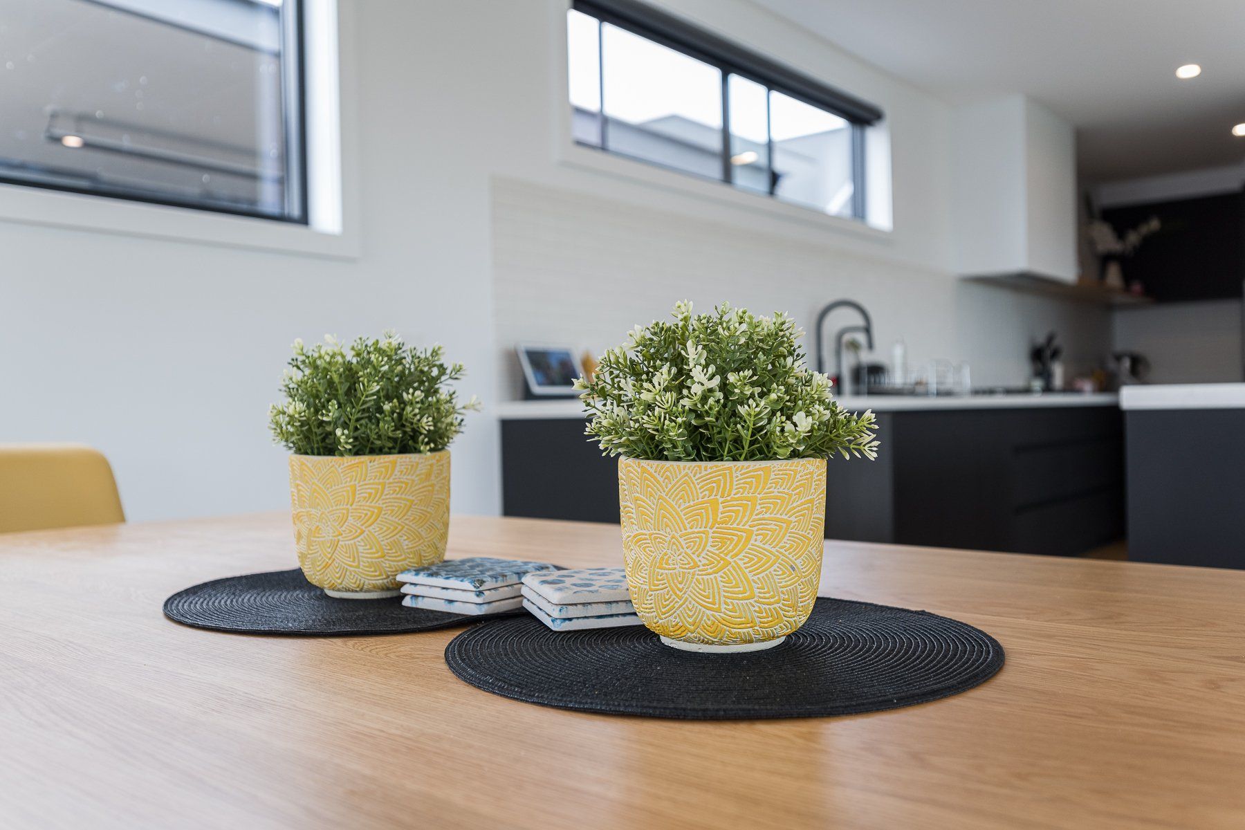 Two potted plants are sitting on a wooden table in a kitchen.